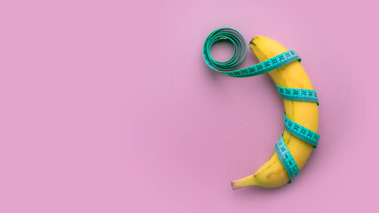 Banana with measuring tape on pink background. Men penis size concept. Flat lay, top view, copy space.