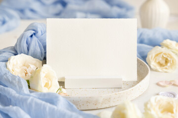 Card near light blue tulle fabric and cream flowers on plate close up, copy space, wedding mockup