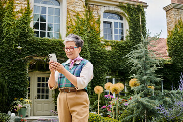 sophisticated joyous mature woman in chic attire looking at her smartphone near her house in England