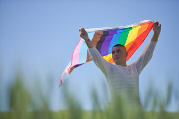Non-binary person, young and South American, very makeup, waving a gay pride flag in the middle of a field of green wheat. Queen of the concept, lgbtq+, pride, queer.
