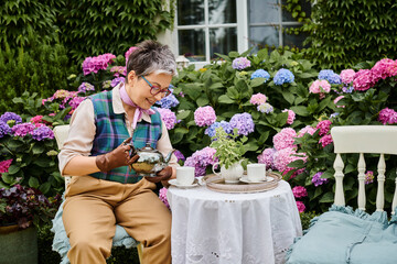 good looking jolly mature woman drinking hot tea at breakfast in garden of her house in England