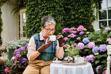 good looking jolly mature woman drinking hot tea at breakfast in garden of her house in England