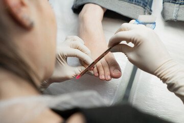 A pedicure master does cleaning and massage, pedicure, to a young beautiful girl with a small foot. Caring for female beauty in a beauty salon during a procedure. Skin of feet and toes close-up