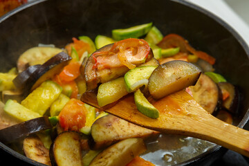 Vegetables fried in spices in a frying pan with a wooden spatula