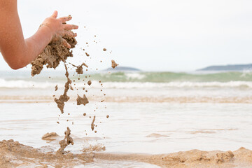 Detail of a kid's hands playing with sand on the beach. Funny and playful. Copy space.