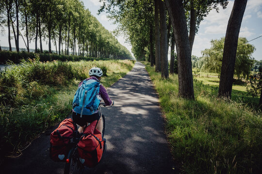 Frau radelt w&auml;hrend einer Radreise auf einem Radweg entlang eines Kanals in Flandern, Belgien