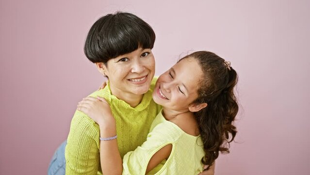 Confident mother and daughter sharing a lovely, happy hug while smiling and standing together over an isolated pink background, expressing a casual lifestyle full of fun, joy and positive vibes.