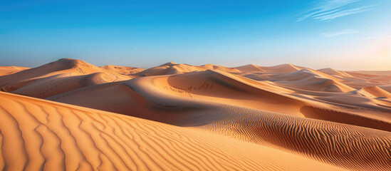 Fototapeta na wymiar Vast desert landscape with undulating golden sand dunes, clear blue sky & hint of footsteps, symbolizing adventure and tranquility