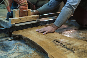 Hands guide wood through a bandsaw, showcasing the art of fine woodworking. It's a blend of control and craftsmanship.