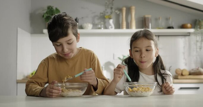 Happy children enjoy eating cereal corn flakes with milk in the kitchen. Kids having breakfast, eating cornflakes with pleasure appetite at home. Cereals corn flakes tasty snack
