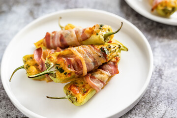 Green paprika appetizer in a plate, green pepper halves stuffed with cheese and wrapped in bacon close up