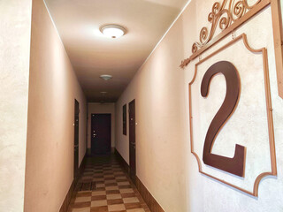 A corridor with wooden doors and a checkered floor pattern. Warmly Lit Hotel Corridor With...