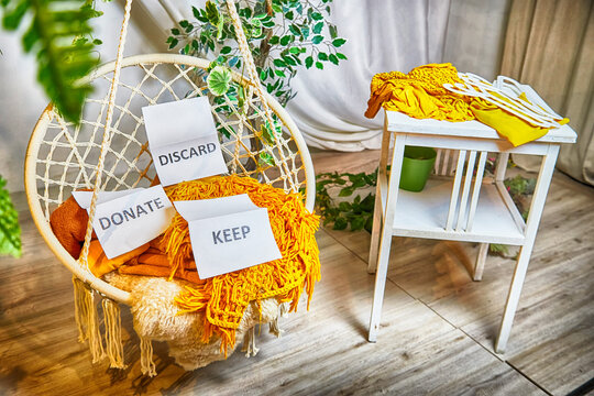 Signs with the words keep, donate, discard and fashion clothes folded in stacks in cozy room. The concept of cluttering, decluttering. Background