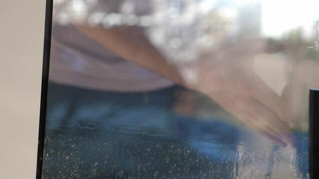 Worker installing and smoothing tint film on window at home. Man tinting windows with squeegee