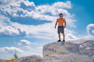 Man stands on large rock against the sky