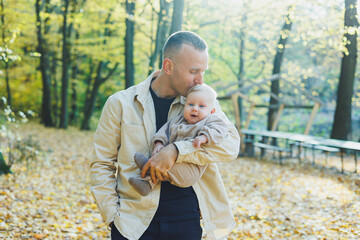 Fototapeta premium Happy young dad hug his little son in the sun on a warm spring or summer day in the park. Sunshine light in the park. Father and son family concept in nature
