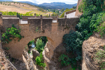 Fototapeta na wymiar View of old stone arched Puente Viejo bridge crossing rocky river in mountainous valley in Ronda, Andalusia, Spain