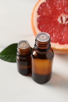 Grapefruit essential oil in bottles, leaf and fruit on white table