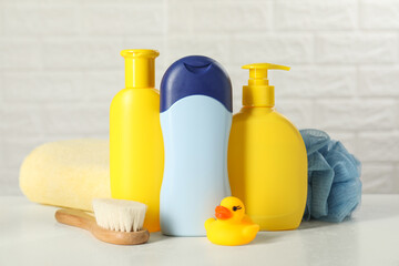 Obraz na płótnie Canvas Baby cosmetic products, bath duck, brush and towel on white table against brick wall