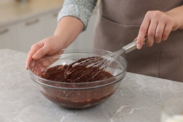 Woman mixing chocolate cream with whisk in bowl at gray marble table indoors, closeup