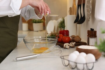 Woman breaking egg at light table in kitchen, closeup