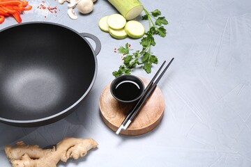 Wok, chopsticks and different products on grey table, space for text