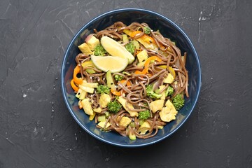 Stir-fry. Delicious cooked noodles with chicken and vegetables in bowl on gray textured table, top view