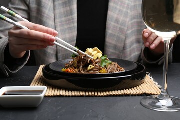 Stir-fry. Woman eating tasty noodles with meat and vegetables at dark textured table, closeup