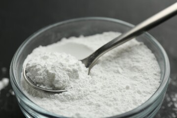 Baking powder in bowl and spoon on black table, closeup