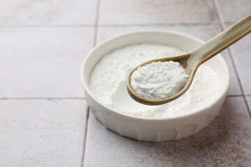 Spoon of baking powder over bowl at light tiled table, closeup. Space for text