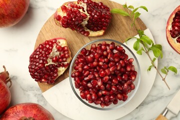 Ripe juicy pomegranate grains and green leaves on white marble table, flat lay