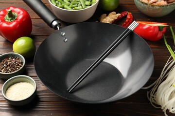 Black wok, chopsticks and products on wooden table, closeup