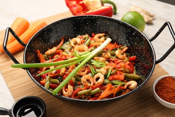 Shrimp stir fry with vegetables in wok and ingredients on wooden table