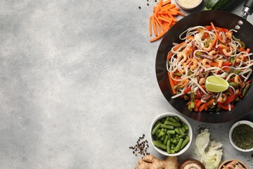 Shrimp stir fry with noodles and vegetables in wok surrounded by ingredients on grey table, flat...