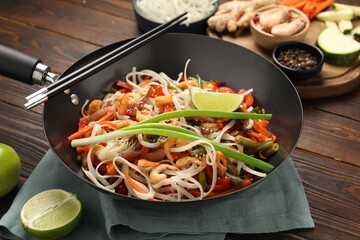 Shrimp stir fry with noodles and vegetables in wok on wooden table