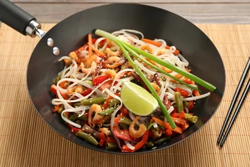 Plexiglas foto achterwand Shrimp stir fry with noodles and vegetables in wok on table © New Africa