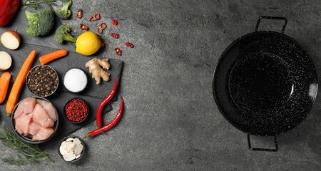 Empty iron wok and raw ingredients on grey table, flat lay. Space for text