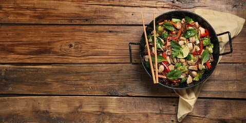 Stir-fry. Tasty noodles with meat in wok and chopsticks on wooden table, top view. Space for text