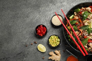 Stir-fry. Tasty noodles with meat in wok, chopsticks and ingredients on grey textured table, flat lay. Space for text