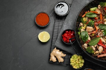 Stir-fry. Tasty noodles with meat in wok and ingredients on grey textured table, flat lay. Space...