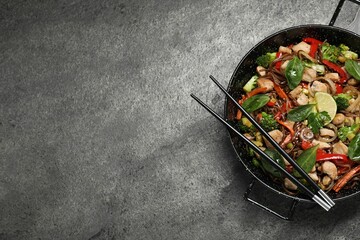 Stir-fry. Tasty noodles with meat in wok and chopsticks on grey textured table, top view. Space for text