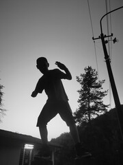 silhouette of young  boy at sunset training yoga or karate. Urban training