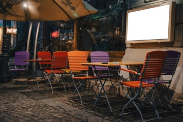 empty white screen television next to the empty table and colorful chairs in the cafe