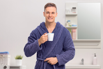 Young man in a blue bathrobe holding a coffee mug and looking at the camera