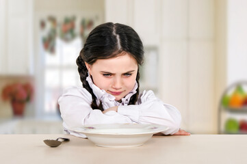 little teenage girl sitting at the dining table in the kitchen. Doesn't eat healthy food. No appetite