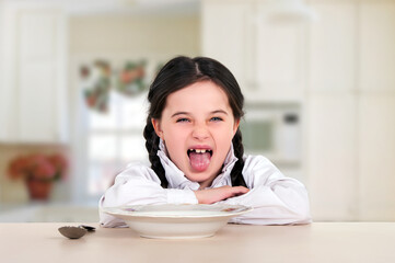 little teenage girl sitting at the dining table in the kitchen. Doesn't eat healthy food. No appetite