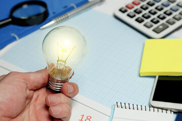 hand holding light bulb in front of desk, business concept - 758333832