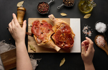 Raw chicken drumsticks seasoned on a wooden board, accompanied by salt and peppercorns