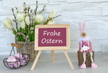 Der Text Frohe Ostern auf eine Tafel geschrieben mit Osterdekoration und Blumen.	