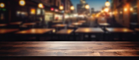 Deurstickers An empty wooden table under a cloudy sky, with a blurry background of a restaurant. The citys horizon and asphalt road blend into the dark landscape © 2rogan